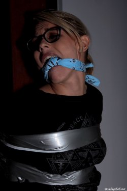 Model Chloe Toy wearing glasses jeans and a t shirt tied up with tape bound to a pole and gagged with a knotted bandanna